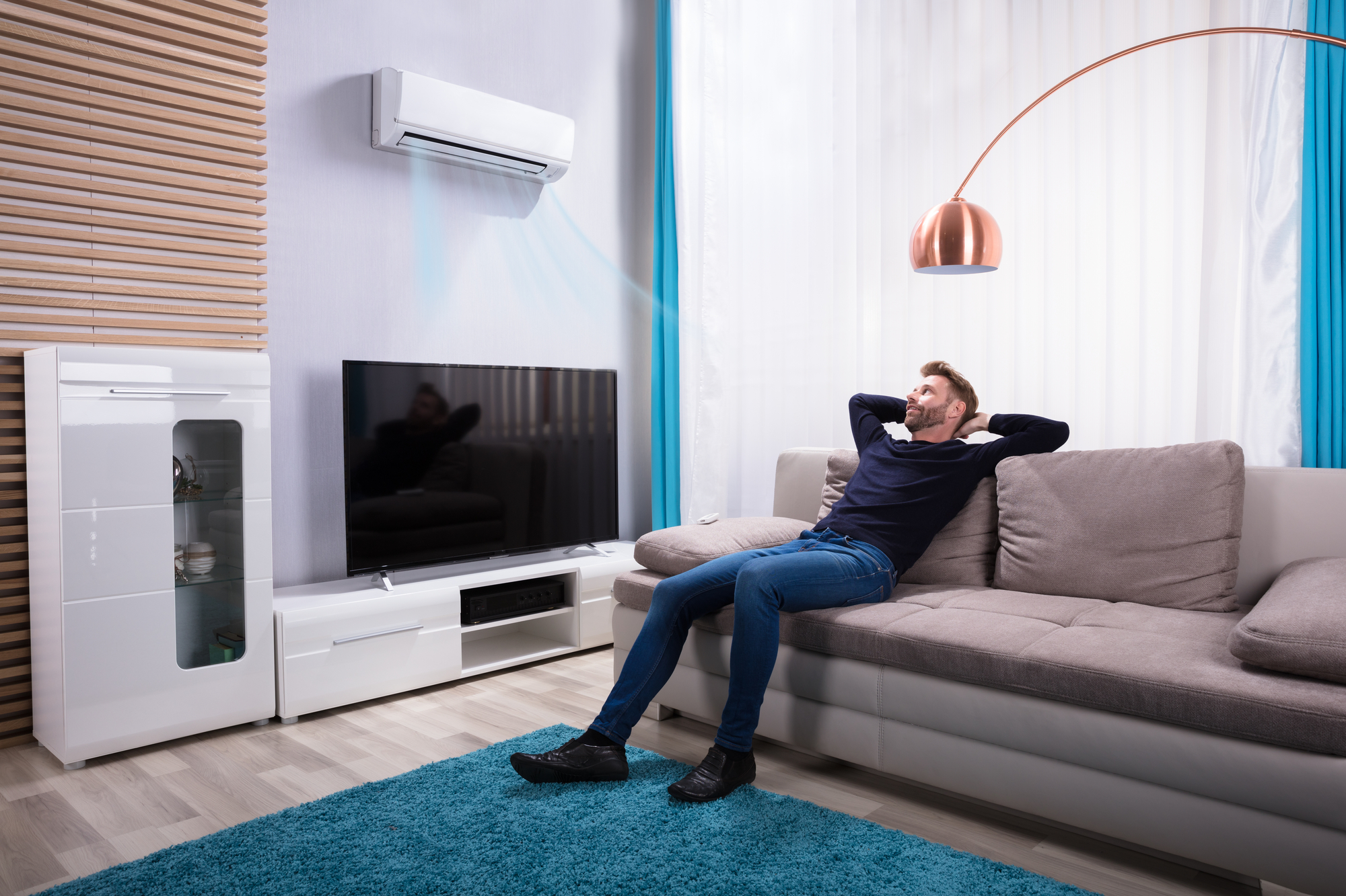 Young Man Relaxing On Sofa With Air Conditioning At Home